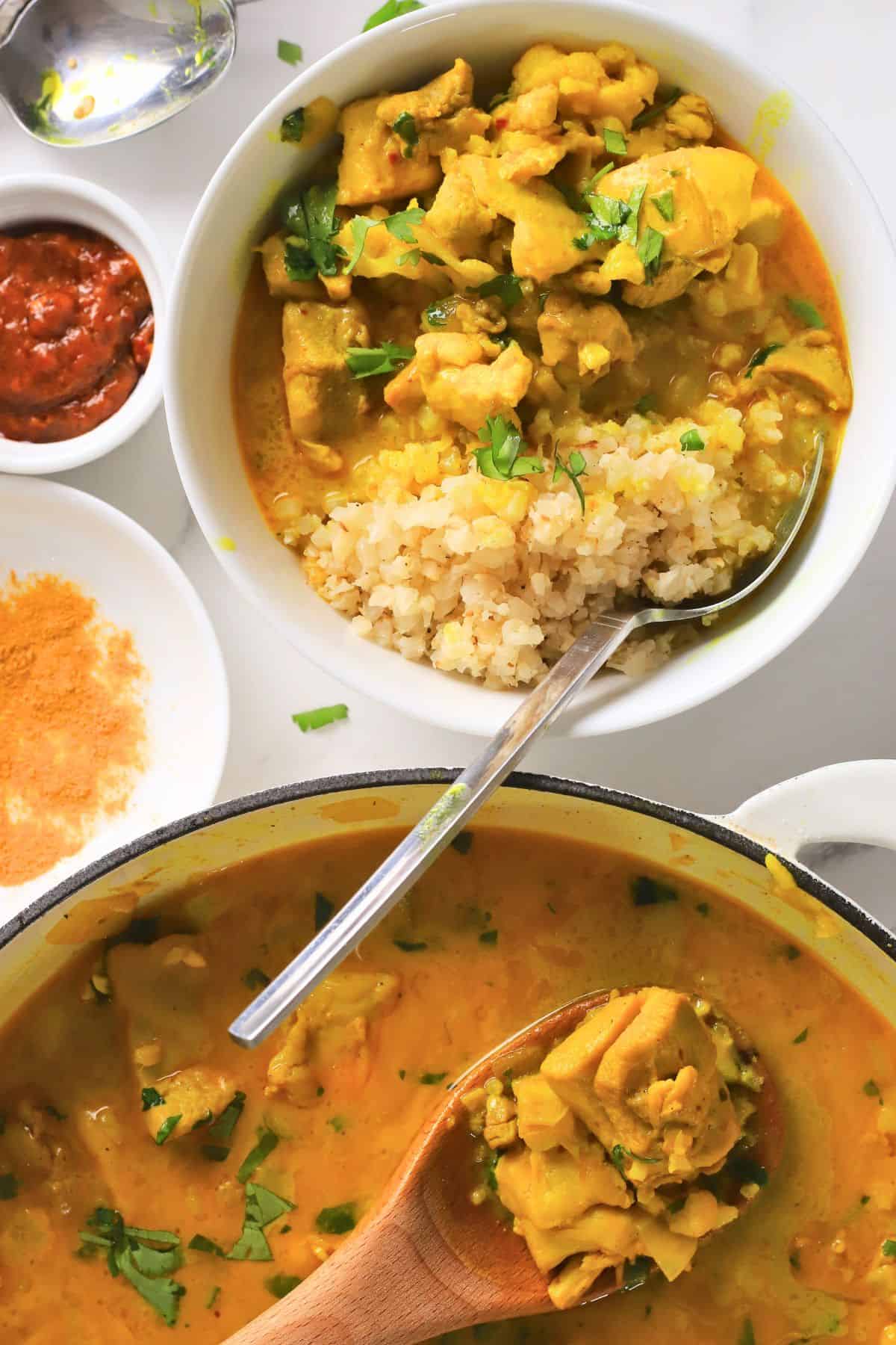 Spooning the low carb thai red curry chicken out of the skillet next to the bowl with the same.