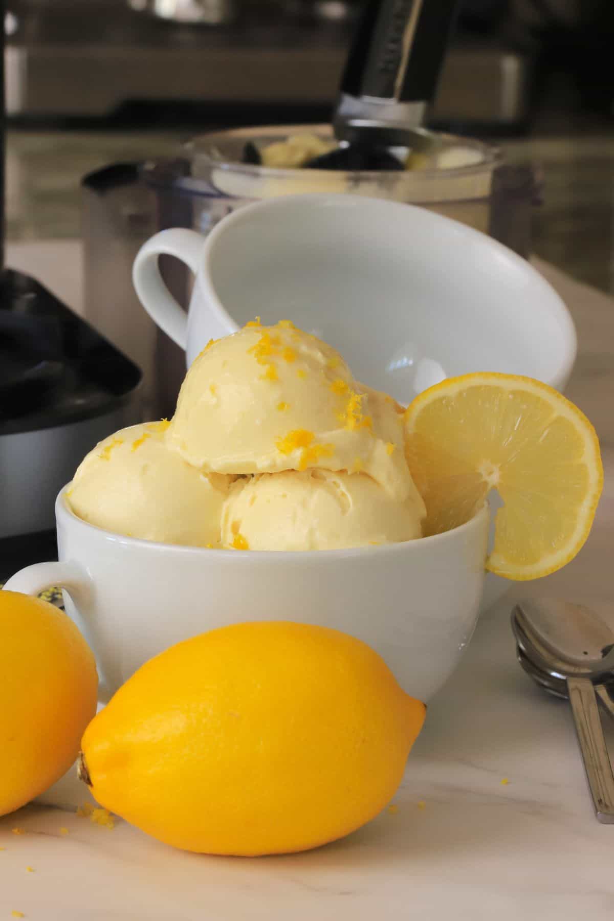 Low carb lemon ice cream in a bowl with a lemon slice next to the ninja creami pint.