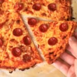Holding a slice of low carb pizza crust on a parchment sheet.