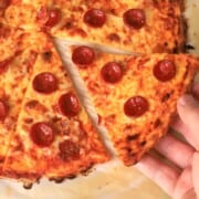 Holding a slice of low carb pizza crust on a parchment sheet.