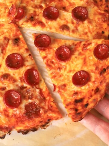 Holding a slice of low carb pizza crust on a parchment sheet.