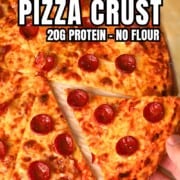 Low carb pizza crust on a parchment sheet while holding a slice.