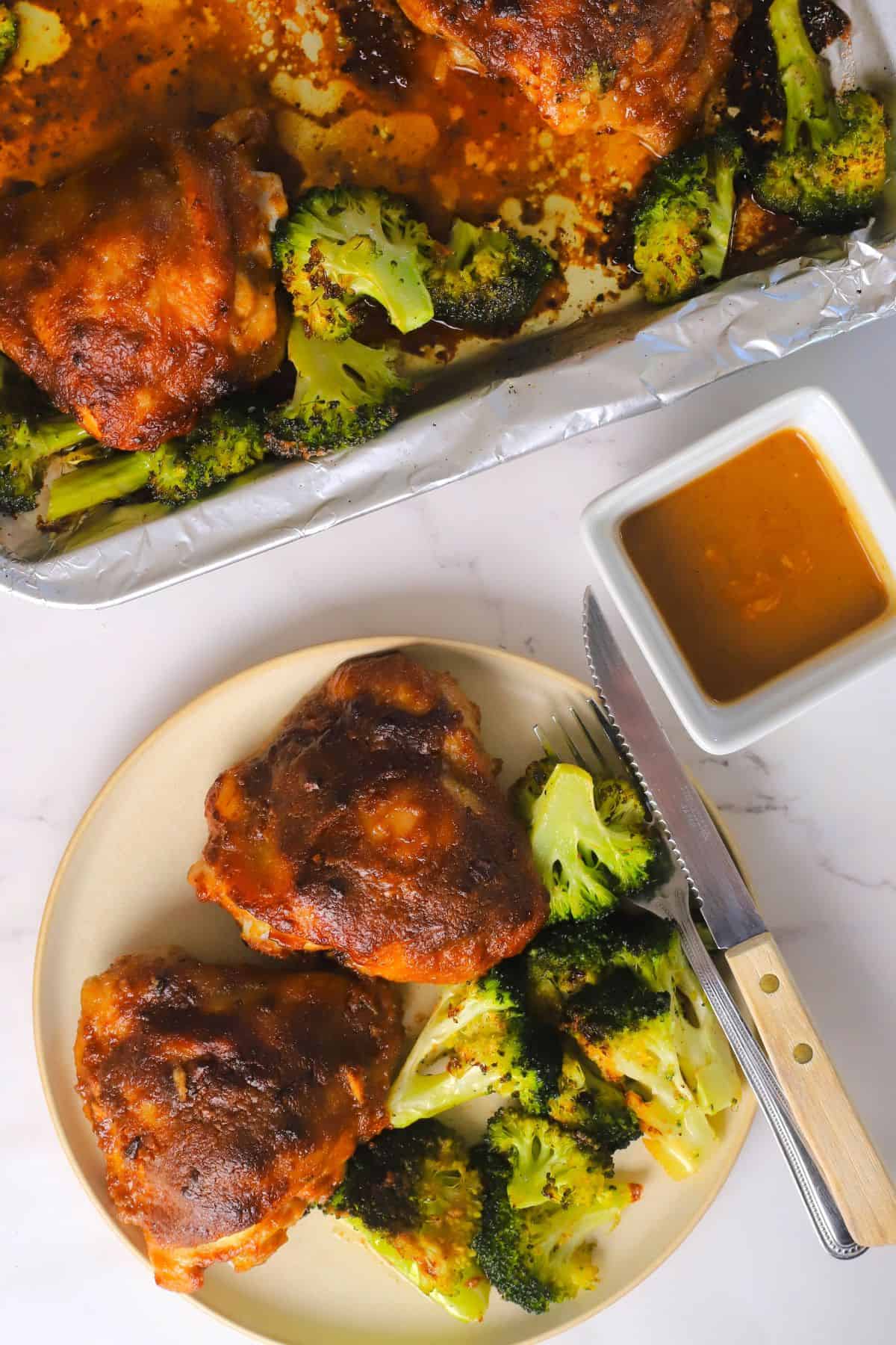 Low carb spicy peanut chicken and broccoli on a plate with the peanut dipping sauce and sheet pan next to it.