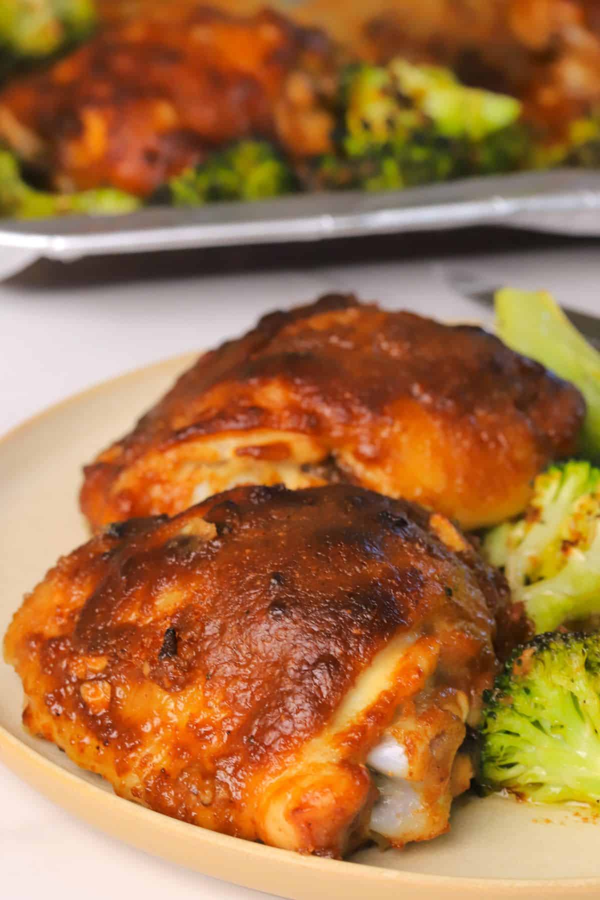 Low carb spicy peanut chicken and broccoli on a plate with the sheet pan in the background.