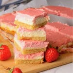 Low carb strawberry cheesecake bars stacked on top of each other next to more sliced bars on a cutting board with fresh strawberries.