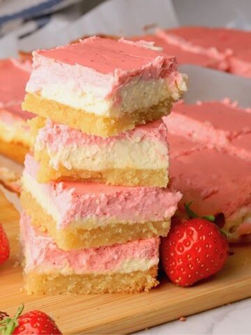 Low carb strawberry cheesecake bars stacked on top of each other next to more sliced bars on a cutting board with fresh strawberries.