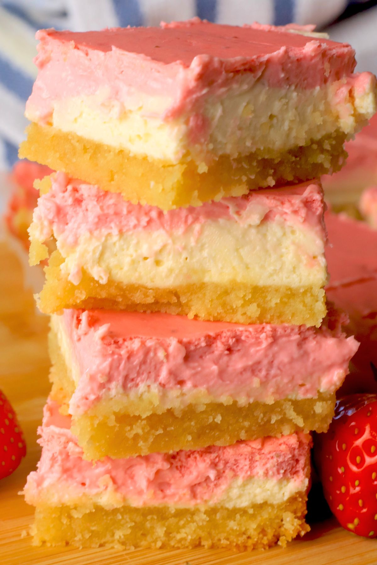 Low carb strawberry cheesecake bars stacked on top of each other next to more sliced bars on a cutting board with fresh strawberries.