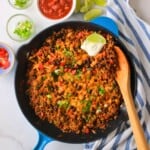 Low carb taco skillet topped with cheese, sour cream and garnished with cilantro and green onions.