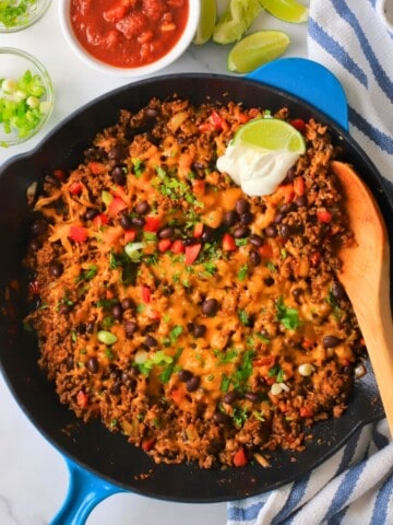 Low carb taco skillet topped with cheese, sour cream and garnished with cilantro and green onions.