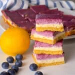 Low carb lemon blueberry cheesecake bars stacked on top of each other next to a lemon and blueberries.
