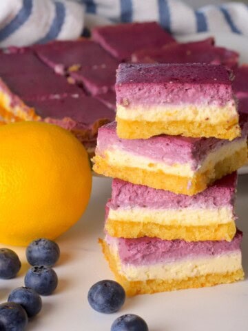 Low carb lemon blueberry cheesecake bars stacked on top of each other next to a lemon and blueberries.