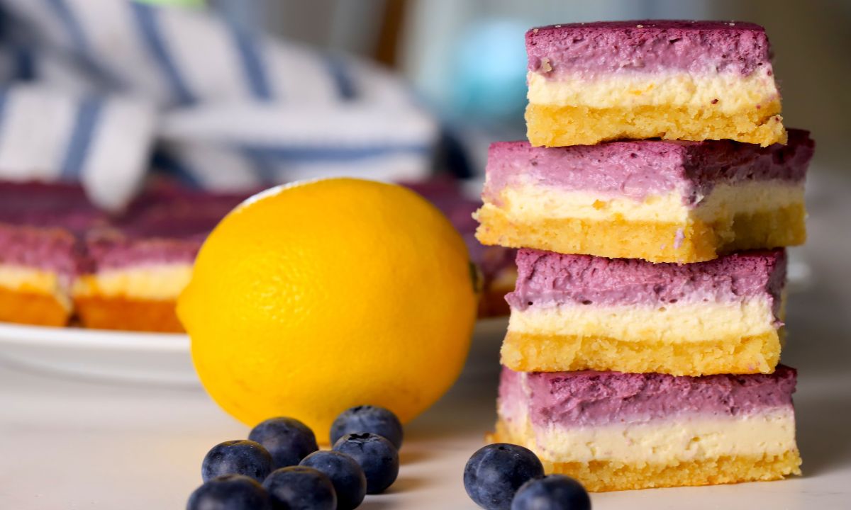 Low carb lemon blueberry cheesecake bars stacked on top of each other next to a lemon and blueberries.