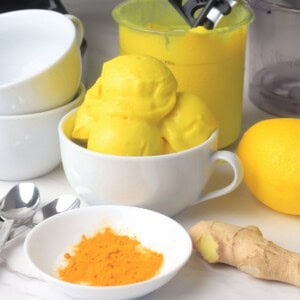 Low carb lemon turmeric ice cream in a bowl next to a lemon, turmeric spices and ginger.