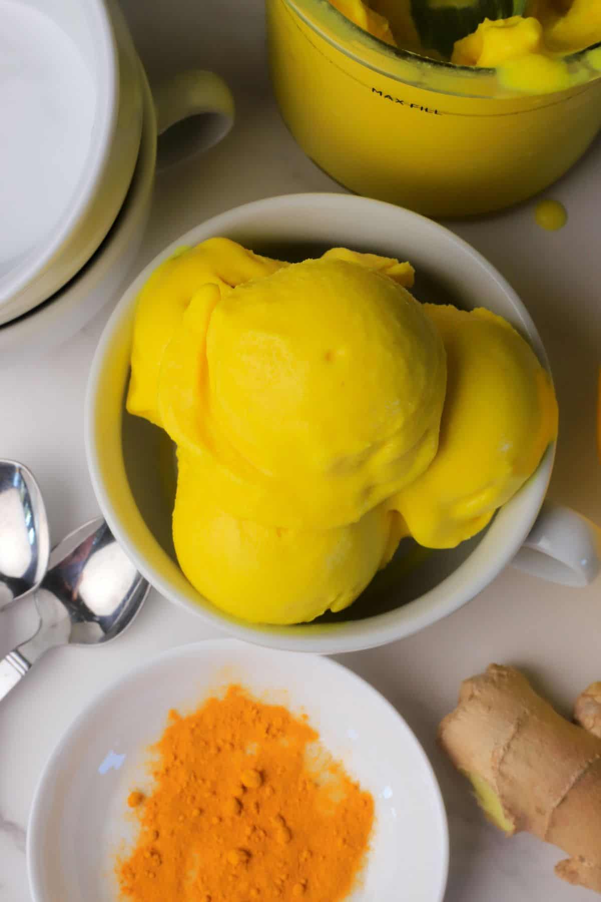 Low carb lemon turmeric ice cream in a bowl next to a lemon, turmeric spices and ginger.