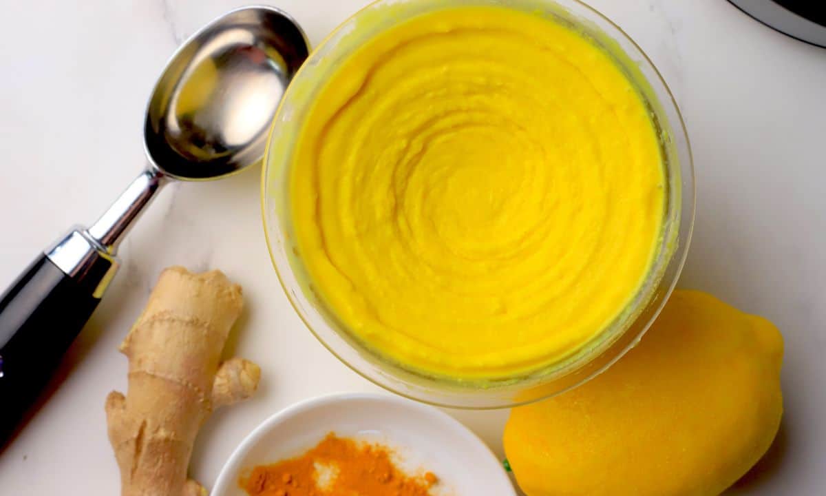 Low carb lemon turmeric ice cream in a the ninja creami pint next to a lemon, turmeric spices and ginger.