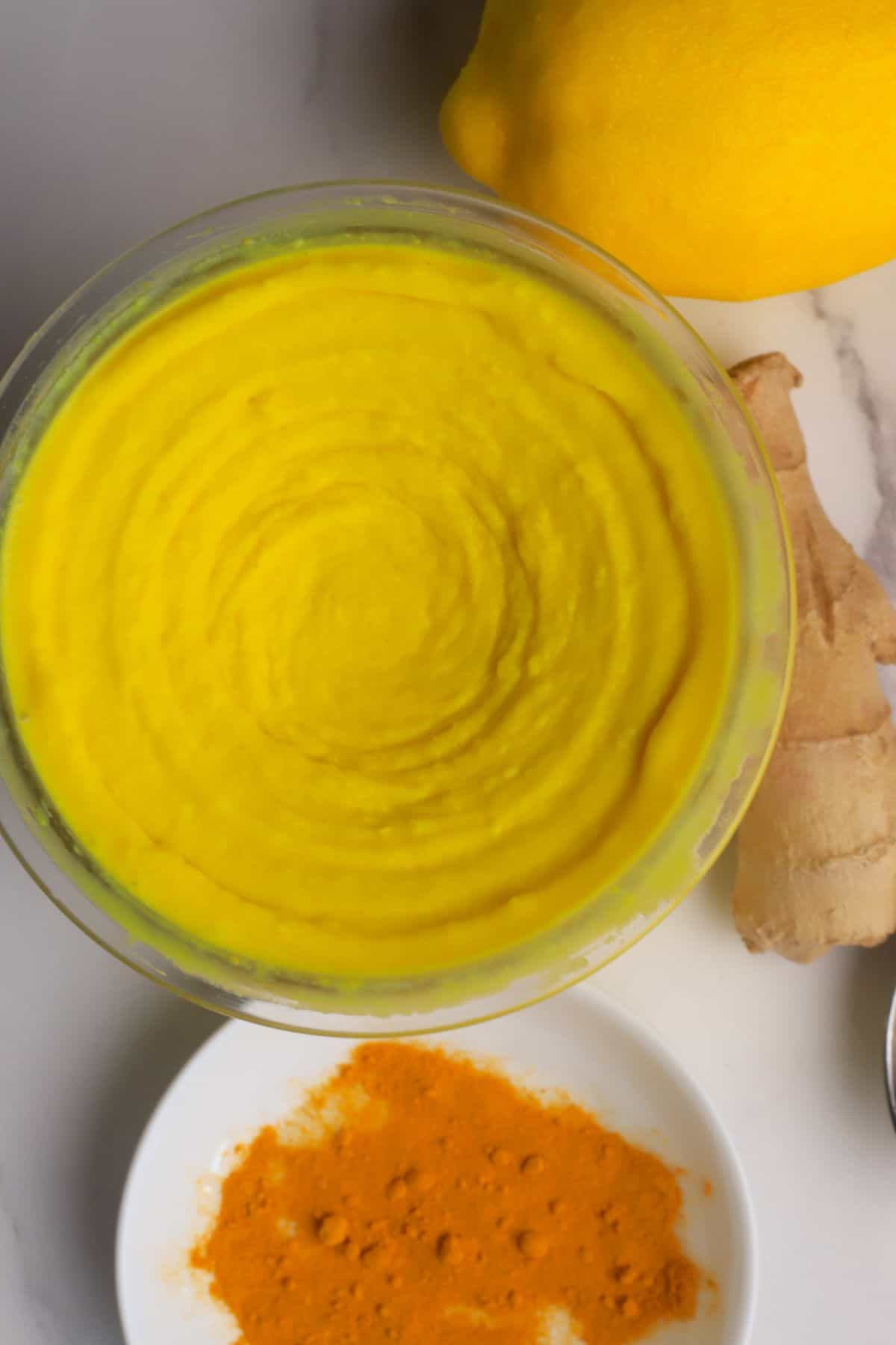 Low carb lemon turmeric ice cream in a the ninja creami pint next to a lemon, turmeric spices and ginger.