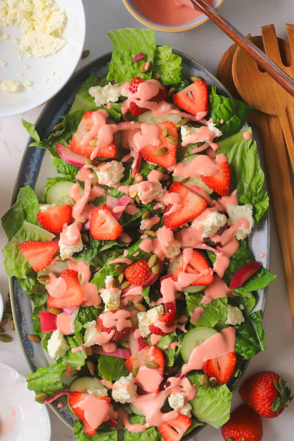 Low carb strawberry feta salad with strawberry dressing next to salad spoons, feta and a bowl with dressing.