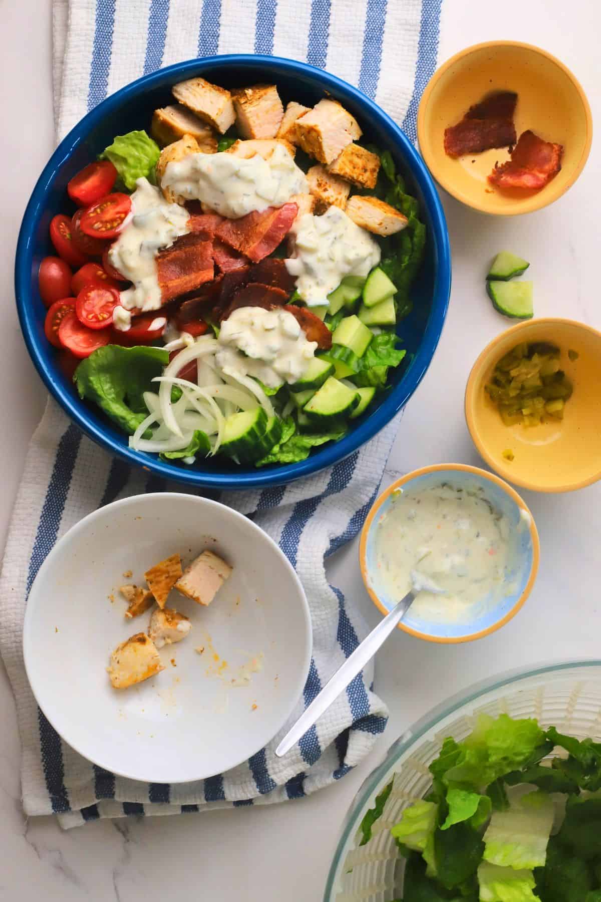 Low carb loaded dill pickle bacon ranch chicken salad in a bowl surrounded by ingredients.