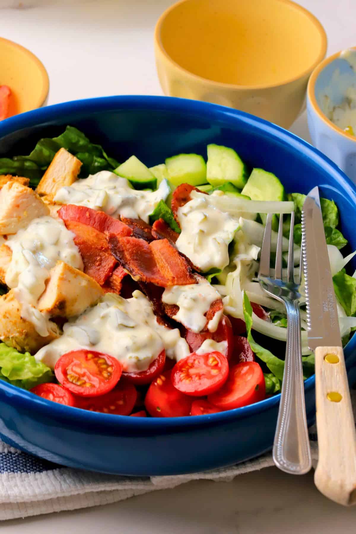 Loaded dill pickle bacon ranch chicken salad in a bowl with a fork and knife.