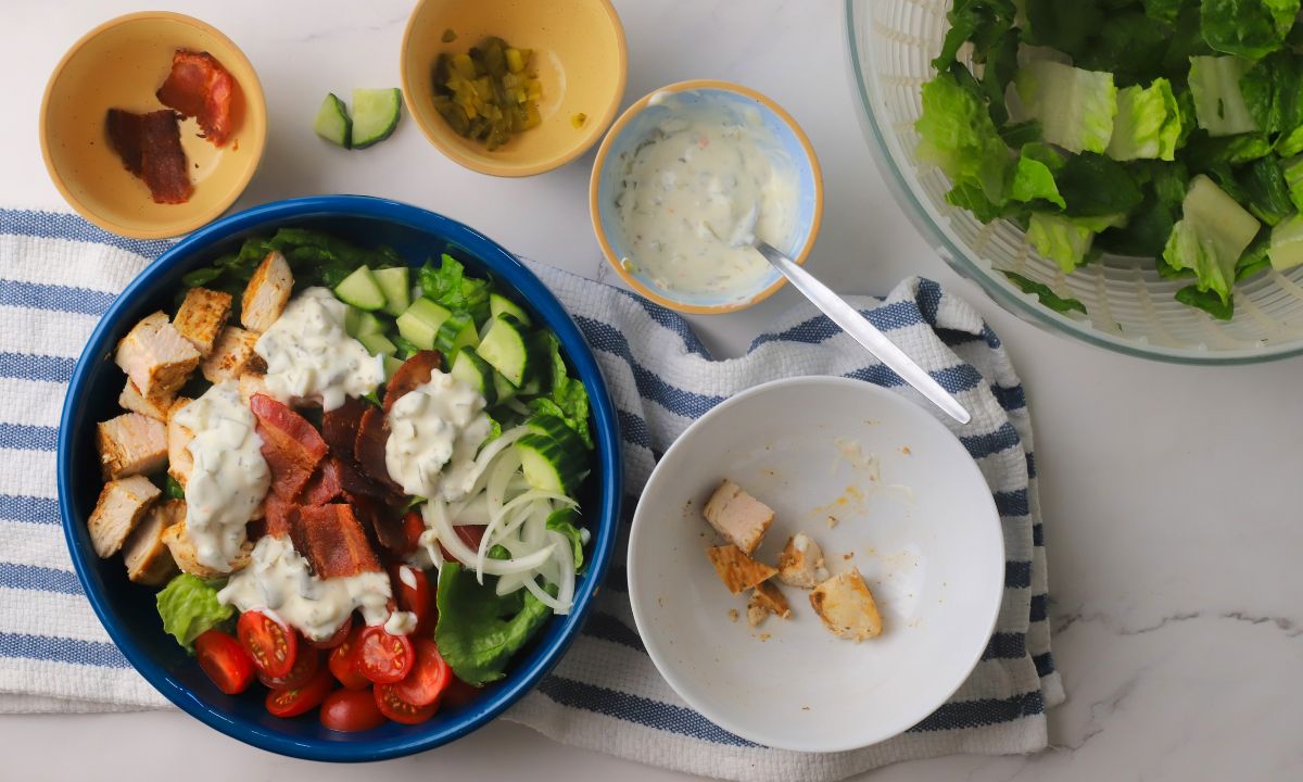 Low carb loaded dill pickle bacon ranch chicken salad in a bowl surrounded buy ingredients.