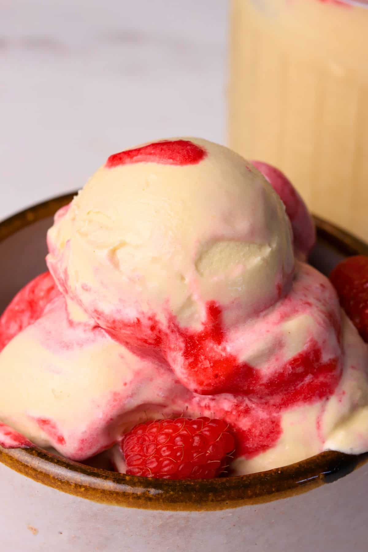 Scoops of low carb peanut butter raspberry ice cream made in the ninja creami in a bowl next to the pint.