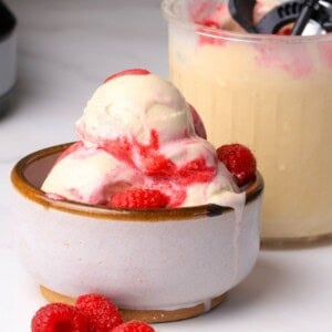 Scoops of low carb peanut butter raspberry ice cream made in the ninja creami in a bowl next to the pint.