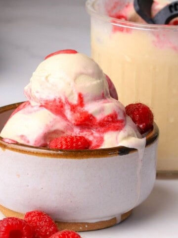 Scoops of low carb peanut butter raspberry ice cream made in the ninja creami in a bowl next to the pint.