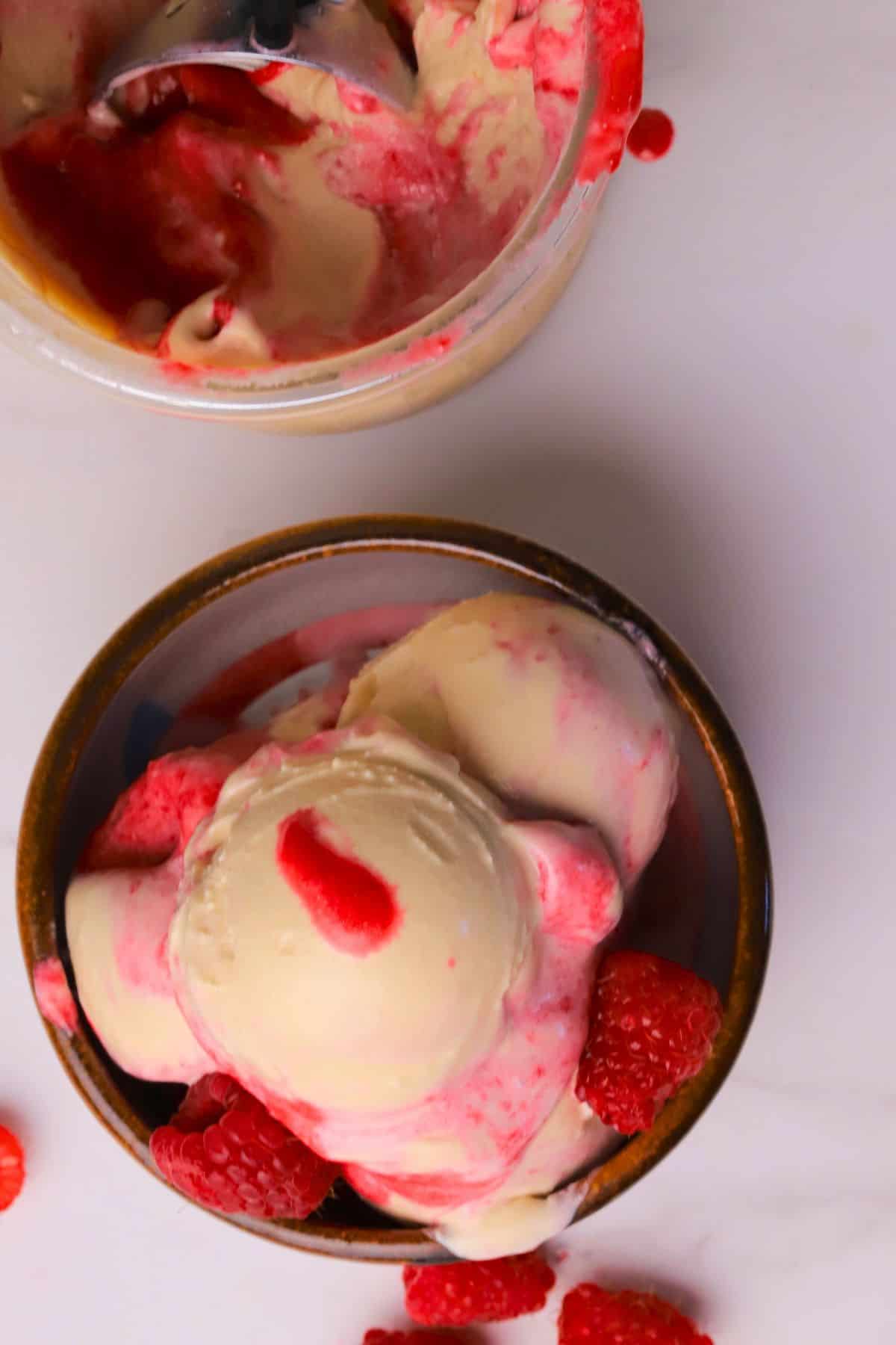 Scoops of low carb peanut butter raspberry ice cream made in the ninja creami in a bowl next to the pint.