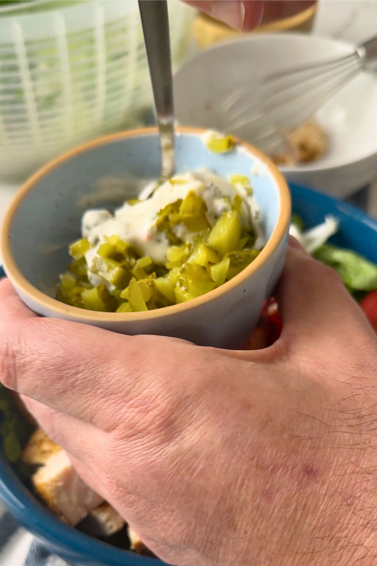 Stirring diced pickles with ranch dressing in a bowl.