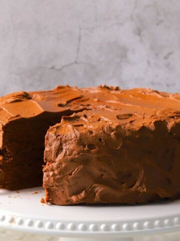 Diabetic chocolate birthday cake on a cake plate with one slice missing.