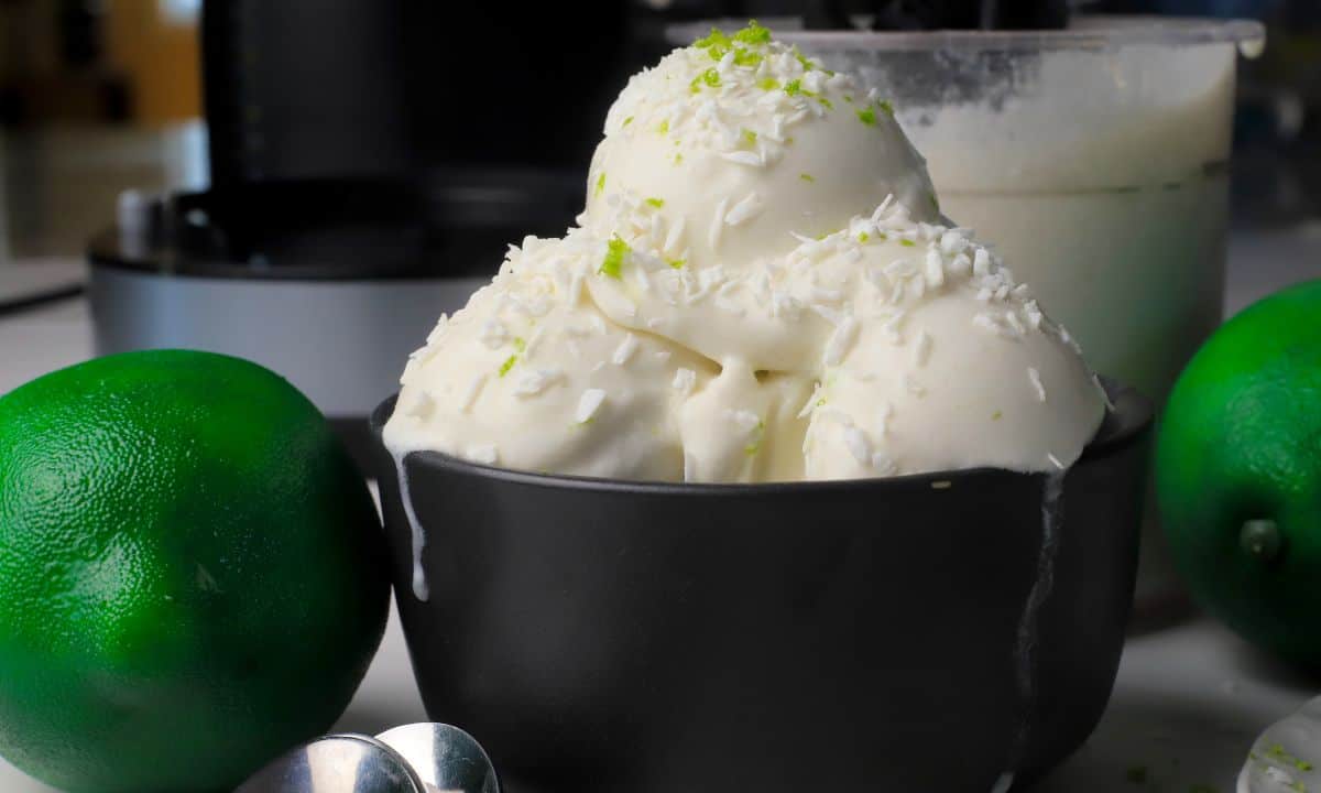 Scoops of low carb coconut lime ice cream in a black bowl with the ninja creami pint in the background with some limes.