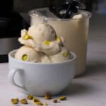 Low carb pistachio almond ice cream in a white bowl next to the ninja creami pint.