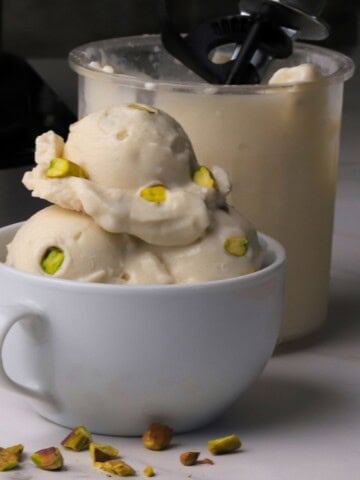 Low carb pistachio almond ice cream in a white bowl next to the ninja creami pint.