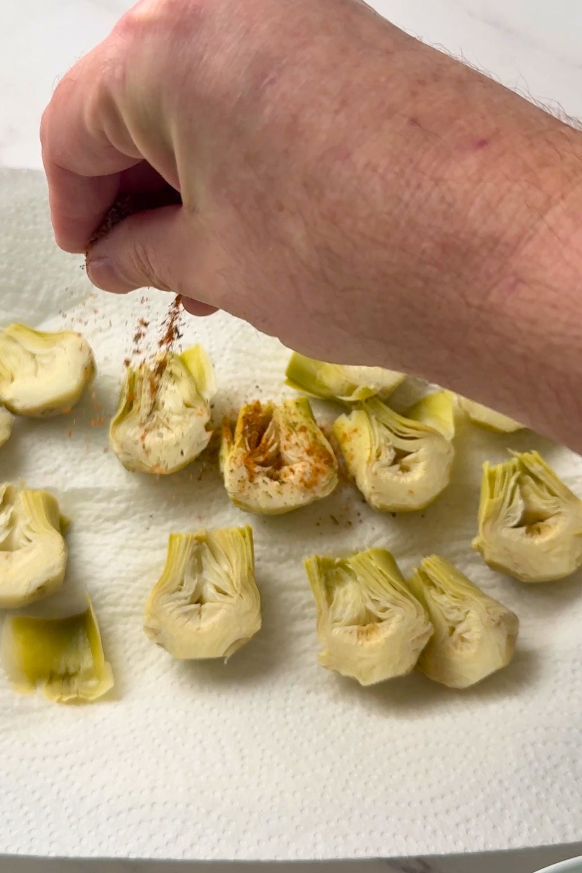 Sprinkling seasonings over artichokes.