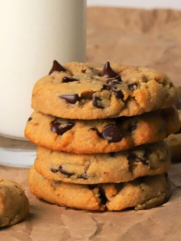 Low carb chocolate chip cookies stacked on top of each other next to a glass of milk.