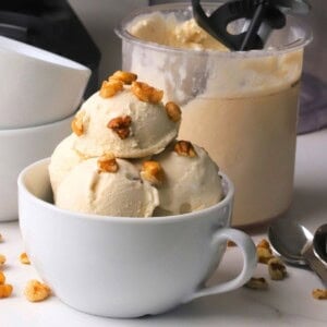 Scoops of low carb maple walnut ice cream in a bowl topped with walnut pieces next to the ninja creami pint.