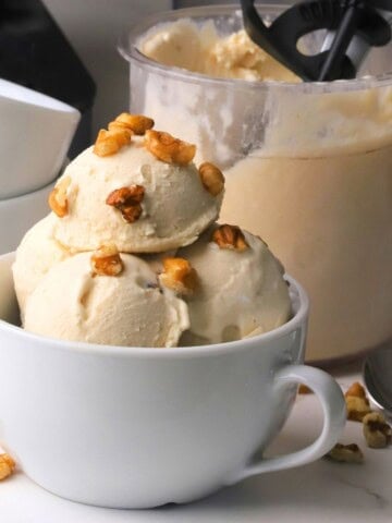 Scoops of low carb maple walnut ice cream in a bowl topped with walnut pieces next to the ninja creami pint.
