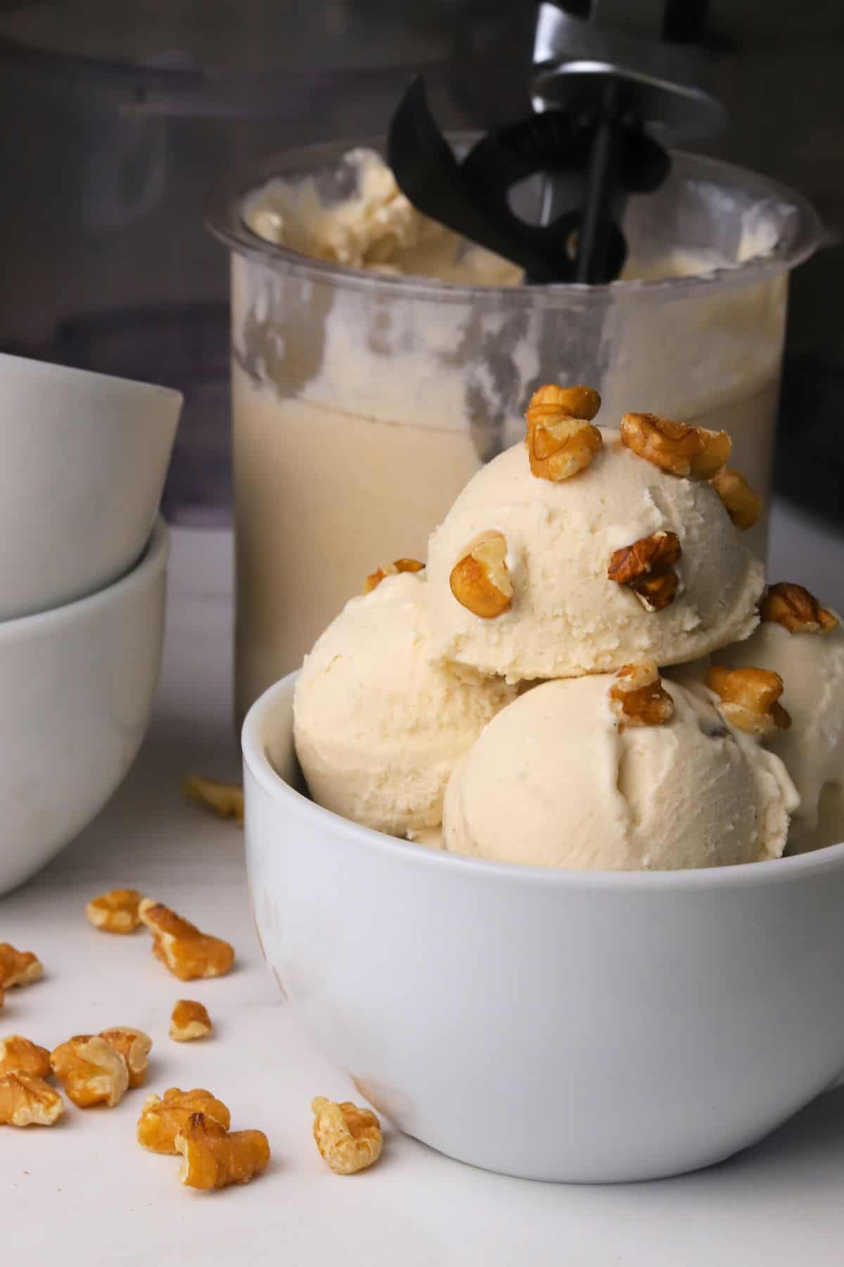 Scoops of low carb maple walnut ice cream in a bowl topped with walnut pieces next to the ninja creami pint.