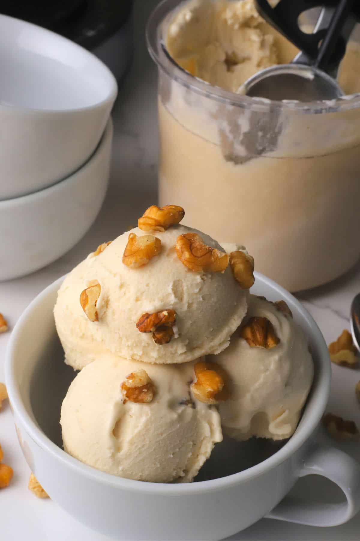 Scoops of low carb maple walnut ice cream in a bowl topped with walnut pieces next to the ninja creami pint.