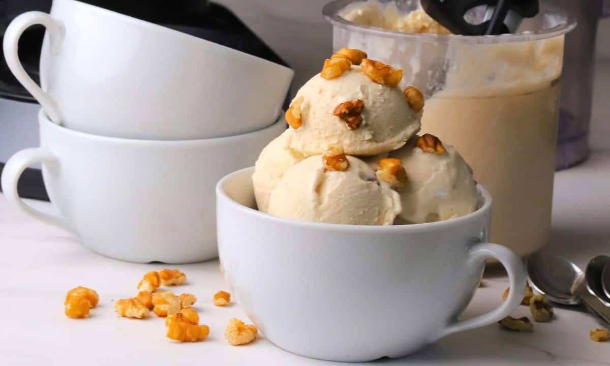 Scoops of low carb maple walnut ice cream in a bowl topped with walnut pieces next to the ninja creami pint.