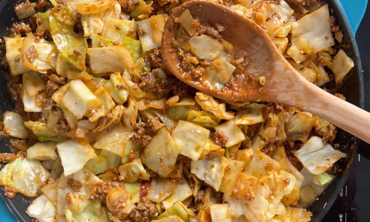 Cabbage beef in a skillet with a wooden spoon.