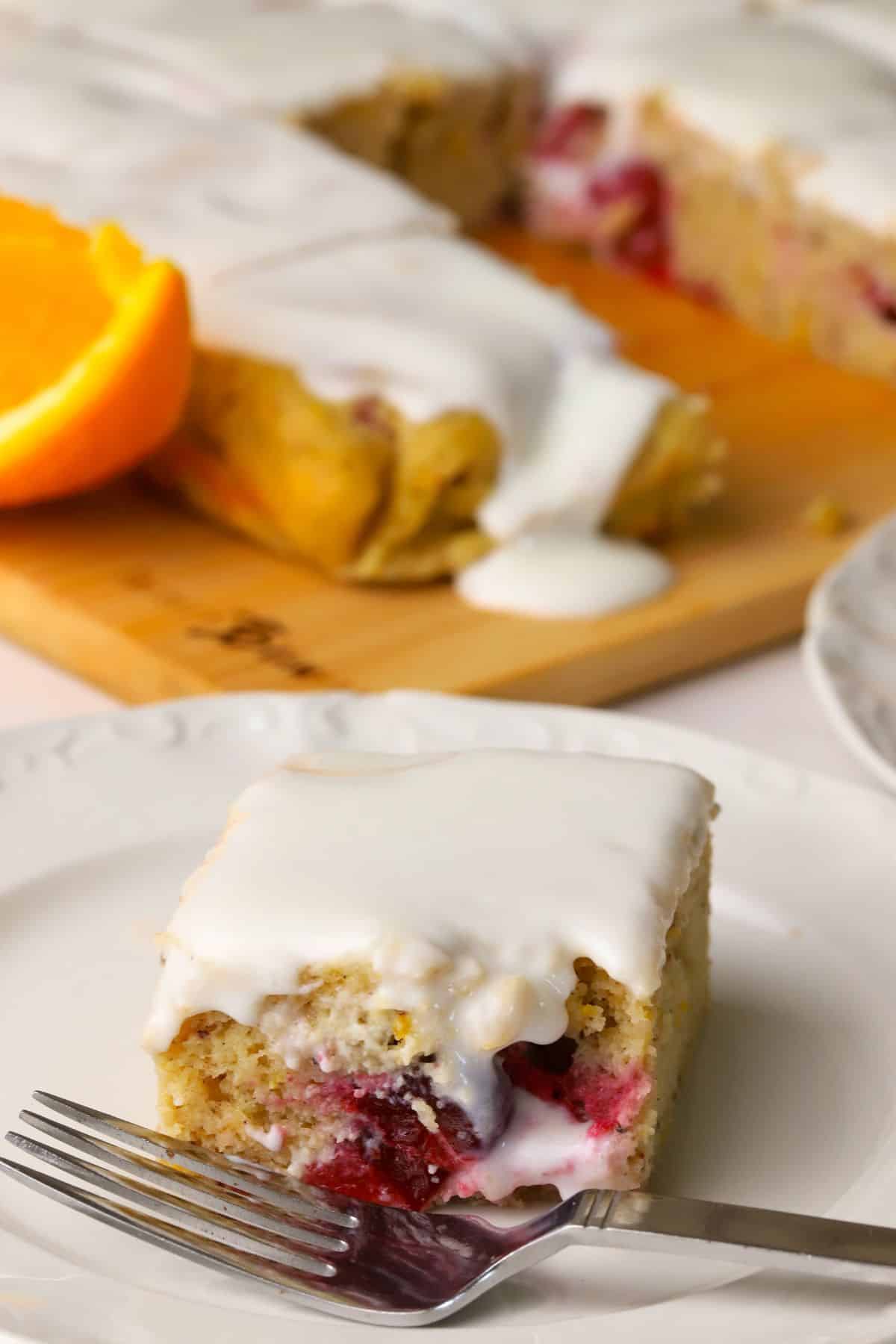 Closeup of a square of the low carb cranberry orange spice cake on a plate with a fork with the cake in the background.