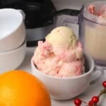 Scoops of low carb cranberry orange spice ice cream in a bowl next to the ninja creami pint and an orange.