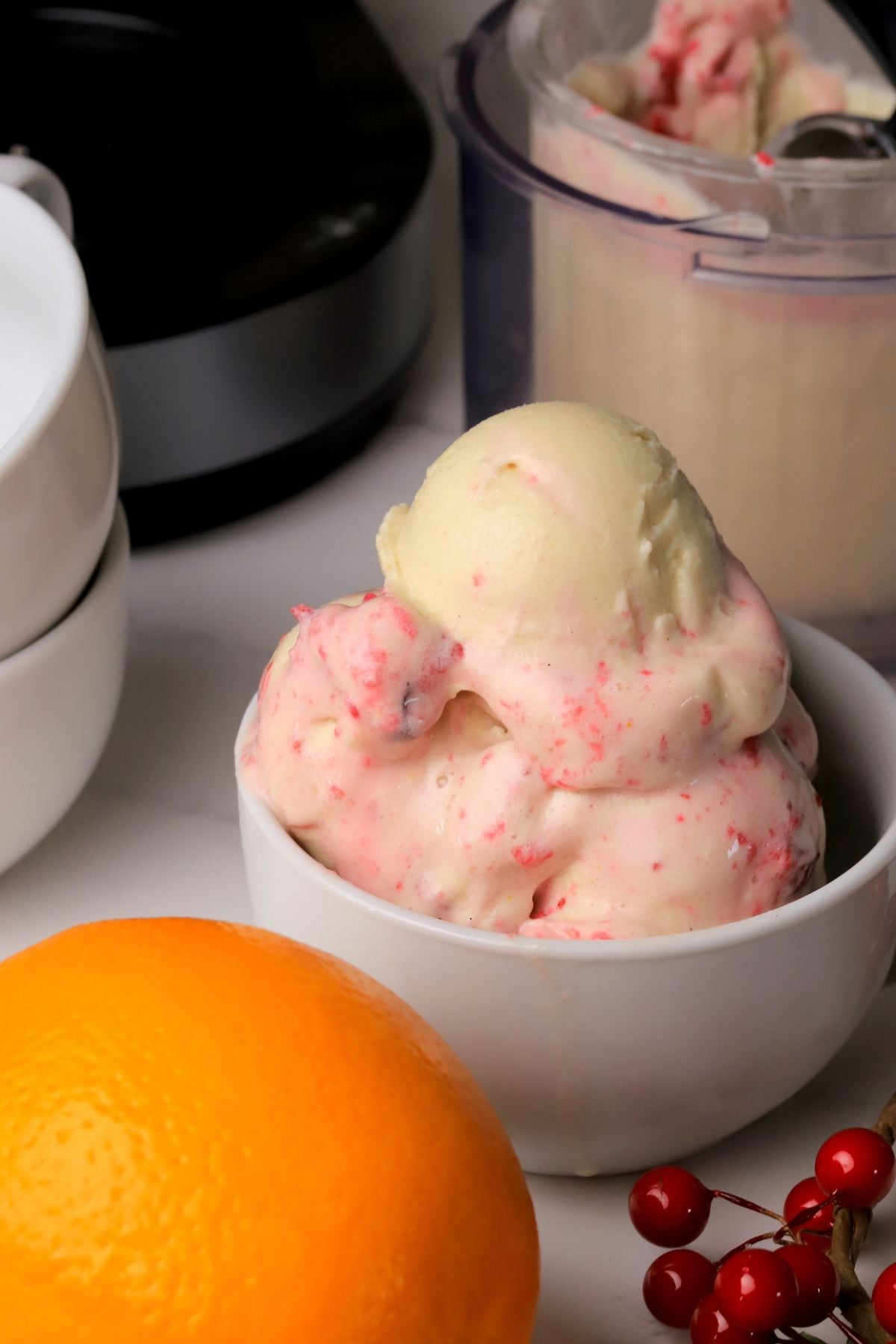 Scoops of low carb cranberry orange spice ice cream in a bowl next to the ninja creami pint and an orange.