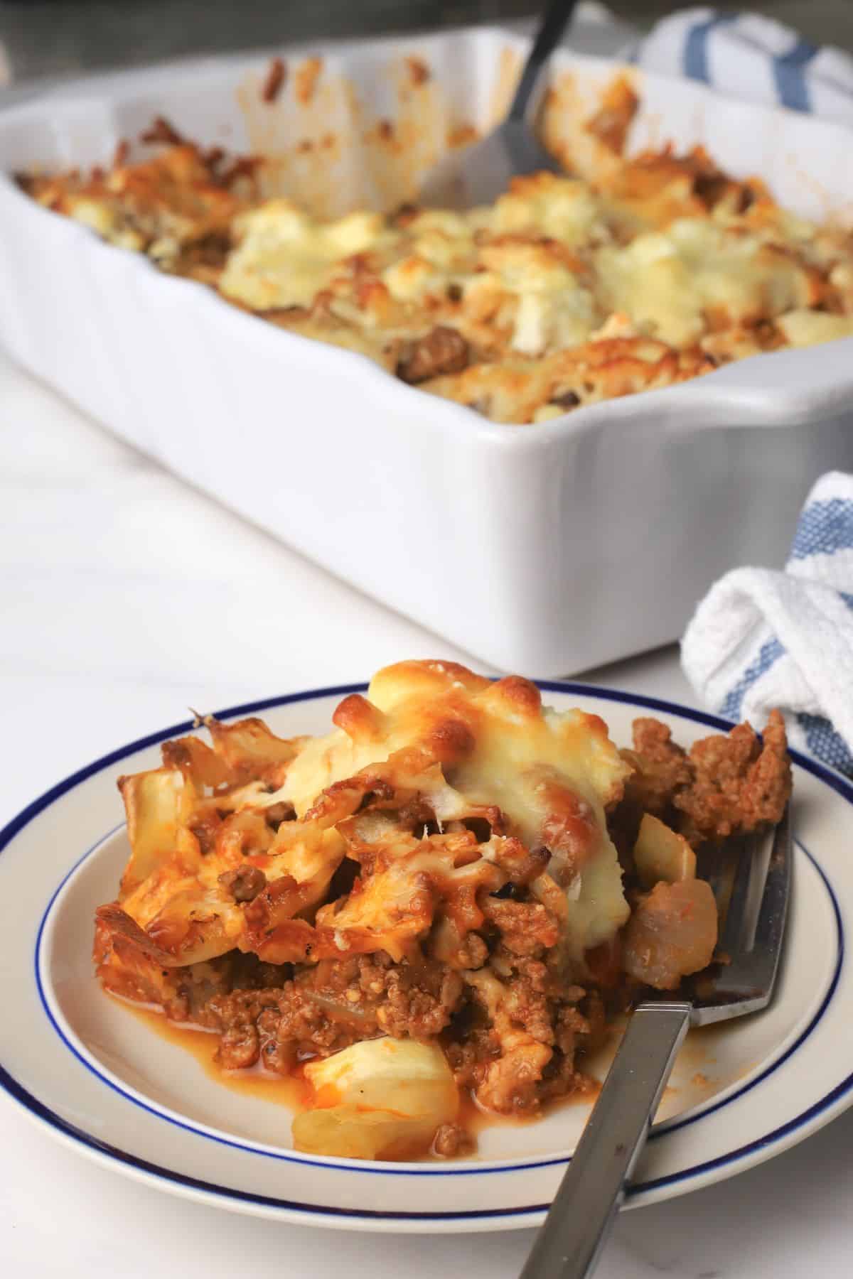 A slice of the low carb italian beef and cabbage cheesy casserole on a plate next to the casserole dish.