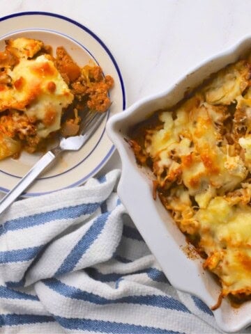 A slice of the low carb italian beef and cabbage cheesy casserole on a plate next to the casserole dish.
