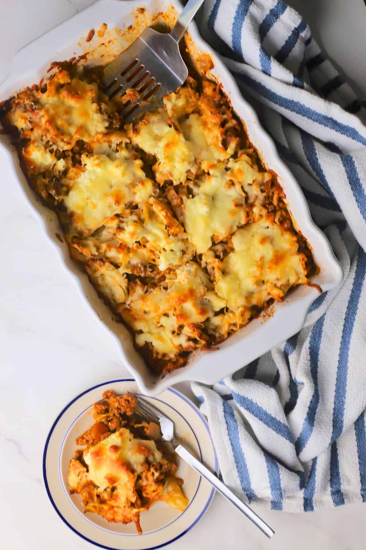 A slice of the low carb italian beef and cabbage cheesy casserole on a plate next to the casserole dish.