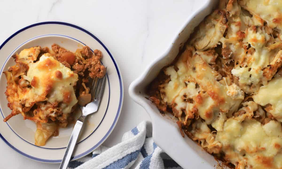 A slice of the low carb italian beef and cabbage cheesy casserole on a plate next to the casserole dish.