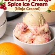 Scoops of low carb cranberry orange spice ice cream in a bowl next to the ninja creami pint and an orange.
