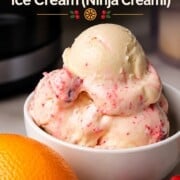 Scoops of low carb cranberry orange spice ice cream in a bowl next to the ninja creami pint and an orange.
